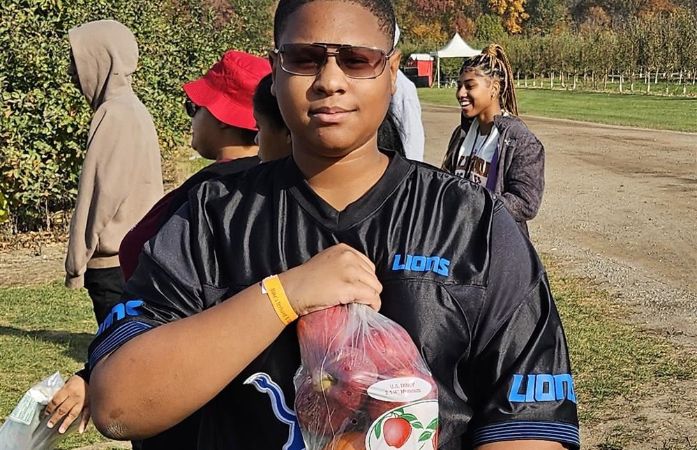  student holding a bag filled with a pumpkin and red apples